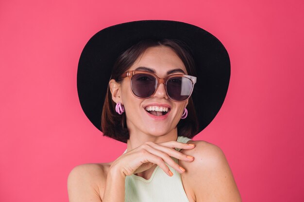 Bella donna alla moda in cappello e occhiali da sole in posa sopra la parete rossa rosa