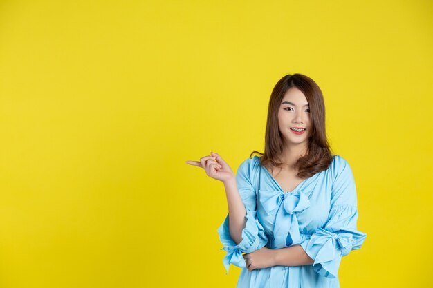 Bella donna asiatica che indica la mano per svuotare lo spazio da parte sulla parete gialla