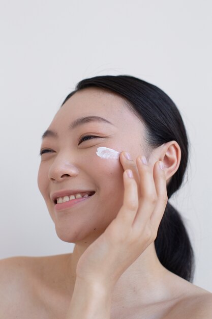 Bella donna asiatica che posa con la crema per il viso