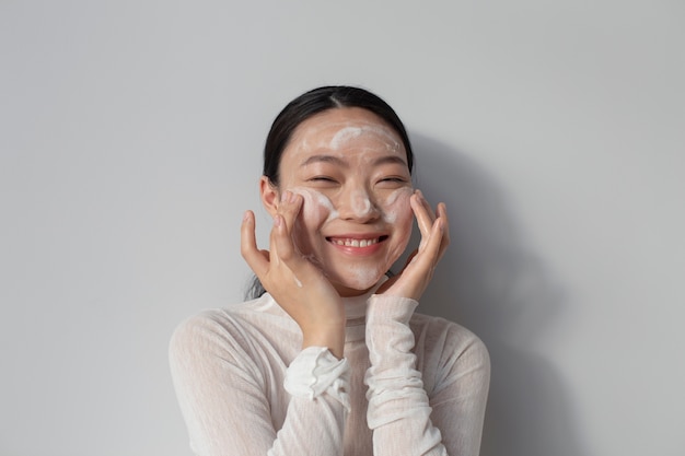 Bella donna asiatica che posa con la crema per il viso