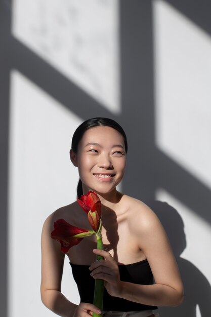 Bella donna asiatica che posa tenendo la rosa con una pelle perfetta