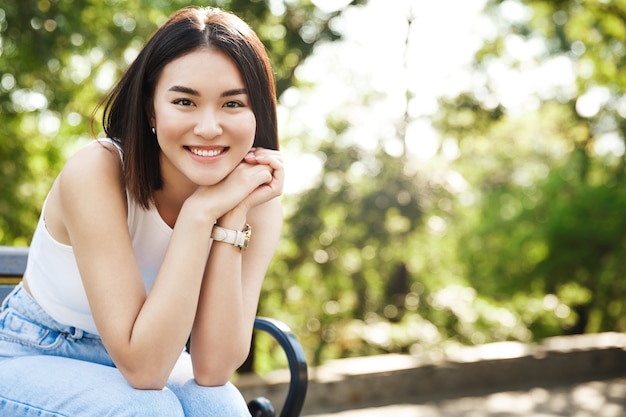 Bella donna asiatica che si siede sulla panchina e sorridente
