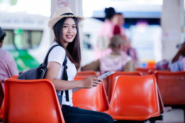 Bella donna asiatica che sorride con la mappa e borsa all&#39;autostazione