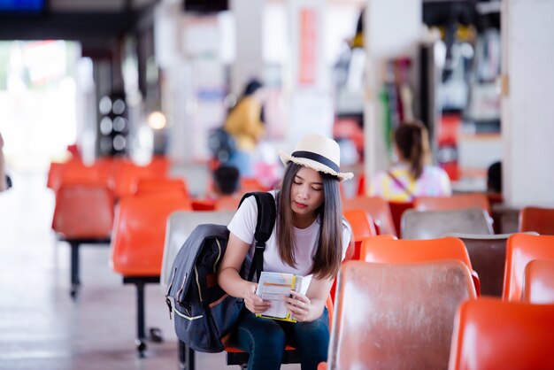 Bella donna asiatica che sorride con la mappa e borsa all&#39;autostazione