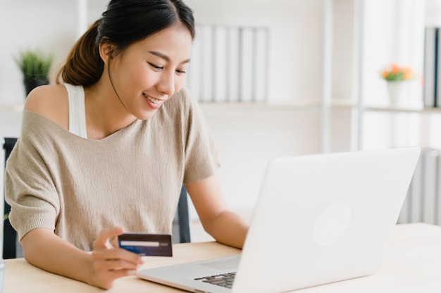 Bella donna asiatica che utilizza computer o computer portatile che compra lo shopping online con carta di credito