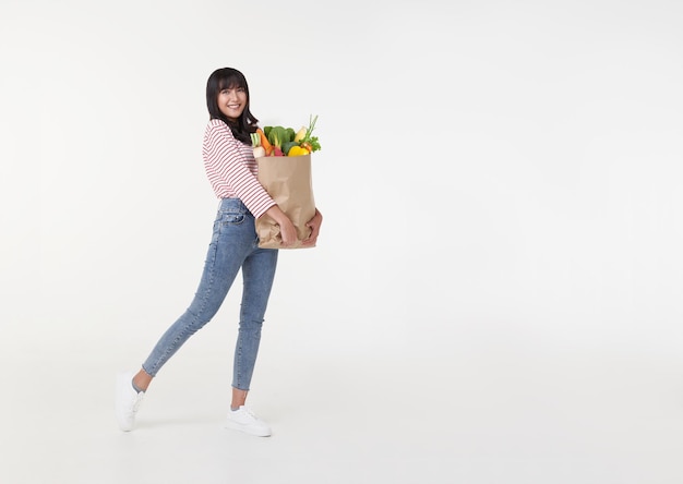 Bella donna asiatica sorridente che tiene il sacchetto della spesa pieno di generi alimentari e cerca di copiare lo spazio da parte