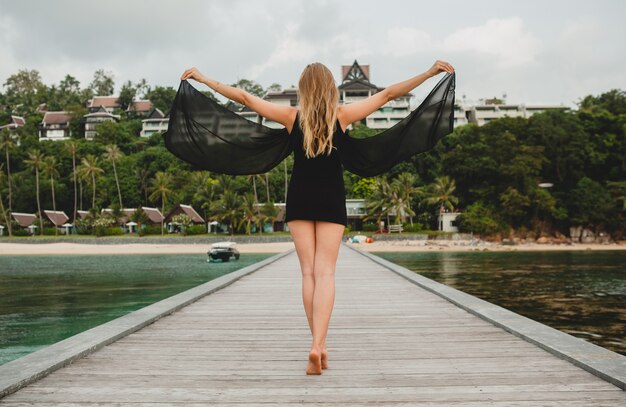 Bella donna attraente vestita in abito nero in posa sul molo in hotel resort di lusso, vacanze estive, spiaggia tropicale