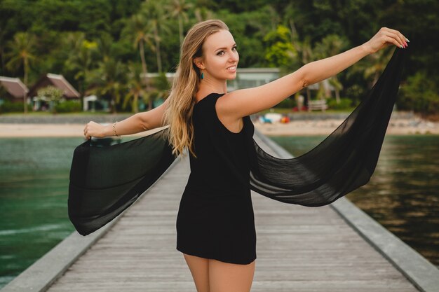 Bella donna attraente vestita in abito nero in posa sul molo in hotel resort di lusso, vacanze estive, spiaggia tropicale