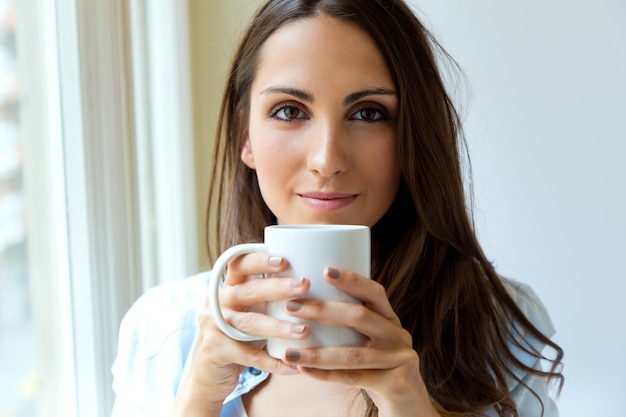 Bella donna bere caffè al mattino vicino alla finestra.