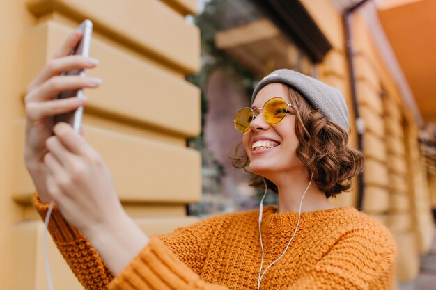 Bella donna bianca con l'acconciatura riccia che fa selfie in vestito nuovo godendo del bel tempo