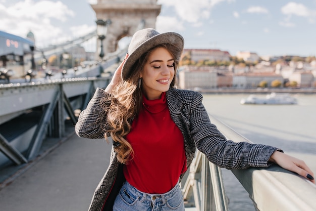 Bella donna bianca indossa un morbido maglione rosso godendo della vista sulla città in viaggio