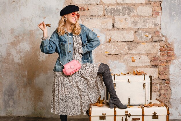 Bella donna bionda alla moda in jeans e giacca oversize in posa contro il muro in strada