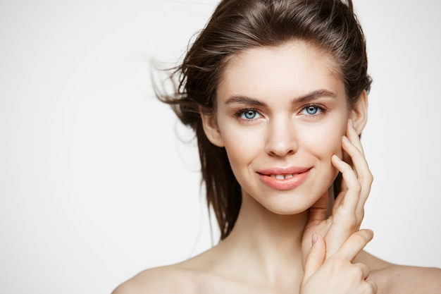 Bella donna bruna con pelle fresca sana e capelli volanti sorridenti toccando il viso.