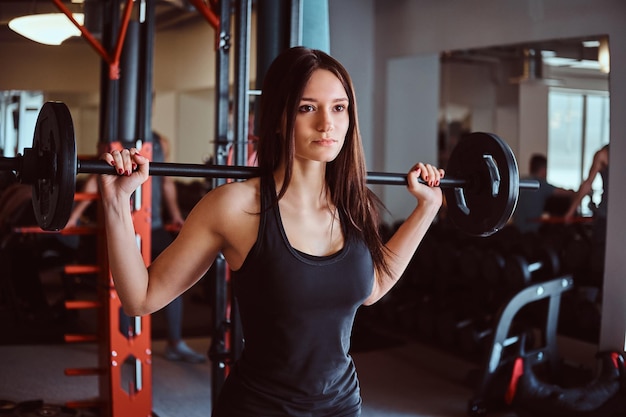 Bella donna bruna in abbigliamento sportivo tiene un bilanciere mentre si allena nel fitness club o in palestra.