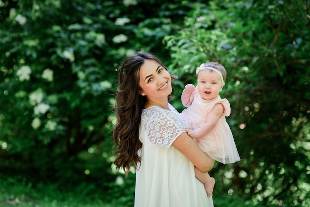 Bella donna bruna in abito bianco pone con la sua figlia in giardino