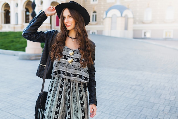 Bella donna castana con l'acconciatura ondulata lunga in primavera o in autunno vestito urbano alla moda che cammina sulla strada. Labbra rosse, corpo magro. Concetto di moda di strada.