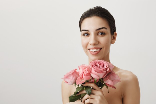 Bella donna castana in piedi nuda con bouquet di rose