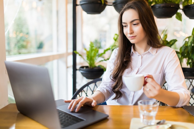 Bella donna caucasica che sogna qualcosa mentre era seduto con net-book portatile nel moderno bar caffetteria. Libero professionista femminile affascinante giovane pensando a nuove idee durante il lavoro sul computer portatile