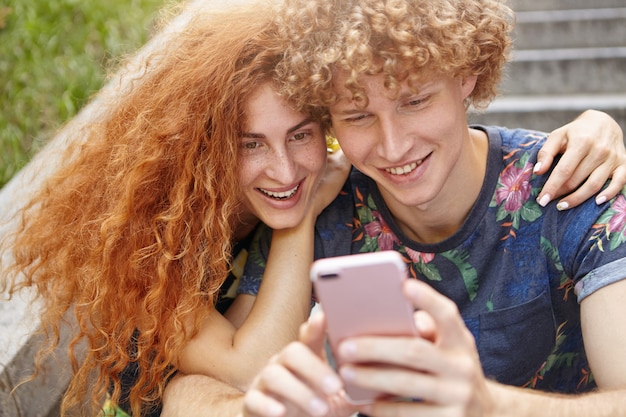 Bella donna che abbraccia il suo ragazzo mentre guarda le loro foto sul cellulare