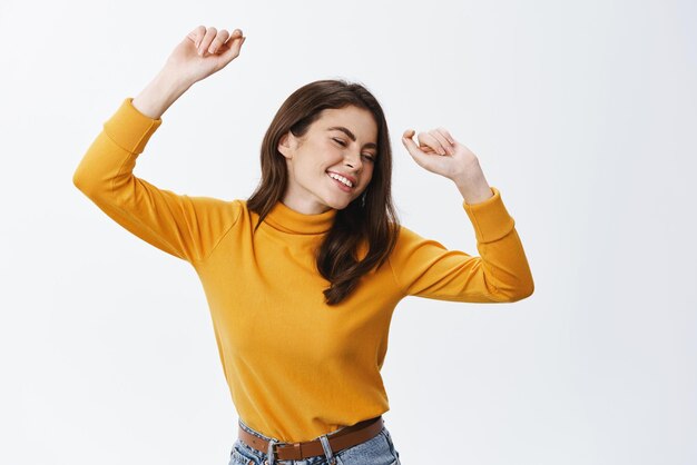 Bella donna che balla e si diverte con gli occhi chiusi e un sorriso spensierato godendosi la festa e la musica in piedi felice su sfondo bianco