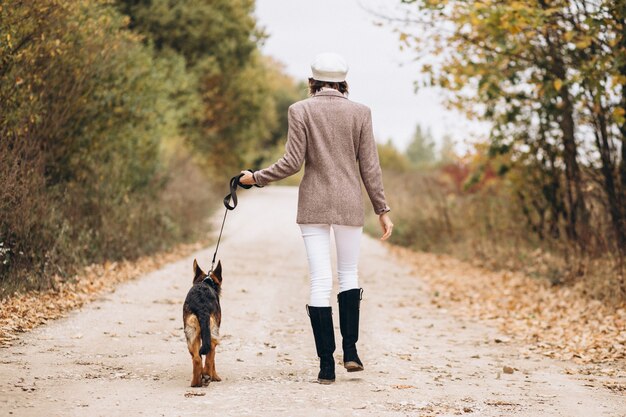 Bella donna che cammina fuori il suo cane nel parco di autunno