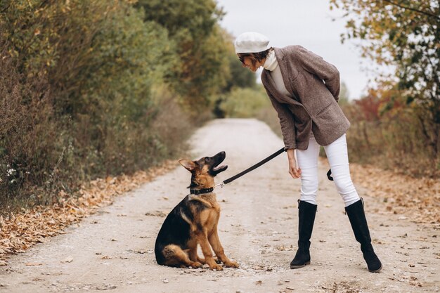 Bella donna che cammina fuori il suo cane nel parco di autunno