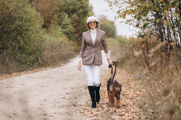 Bella donna che cammina fuori il suo cane nel parco di autunno