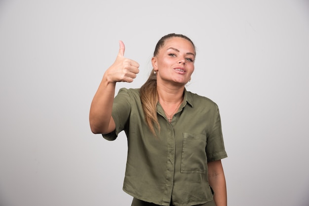 Bella donna che dà i pollici in su sul muro grigio.