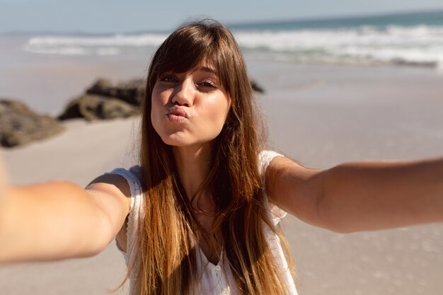 Bella donna che fa il broncio mentre esaminando macchina fotografica sulla spiaggia al sole