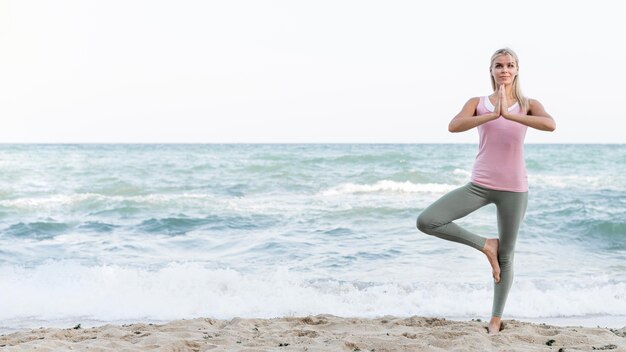 Bella donna che fa yoga in spiaggia