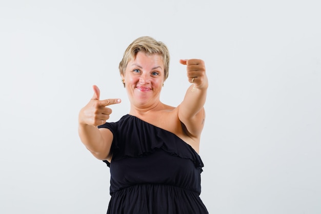 Bella donna che indica alla sua mano sinistra in camicetta nera e che sembra soddisfatta