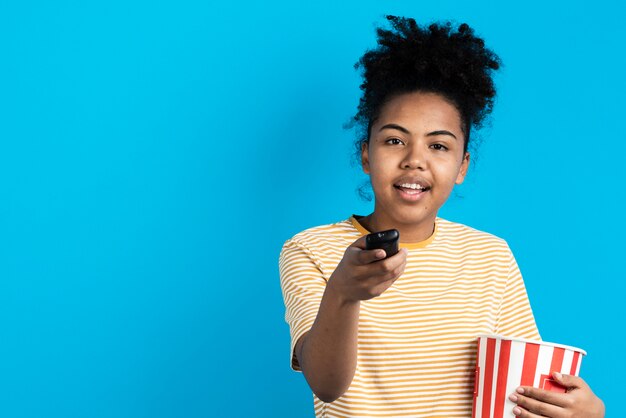 Bella donna che indica telecomando con il secchio del popcorn