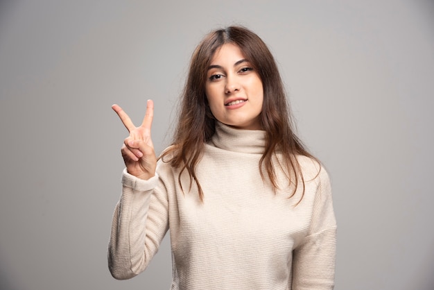 Bella donna che indossa un maglione casual che mostra e punta verso l'alto con le dita numero due mentre sorride.
