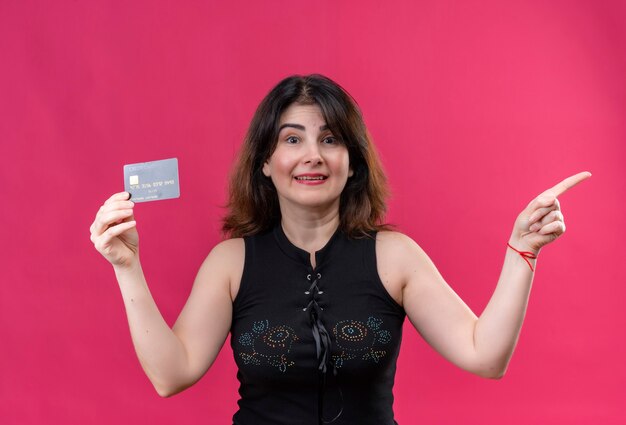 Bella donna che indossa una camicetta nera che guarda felicemente tenendo la carta che punta a sinistra