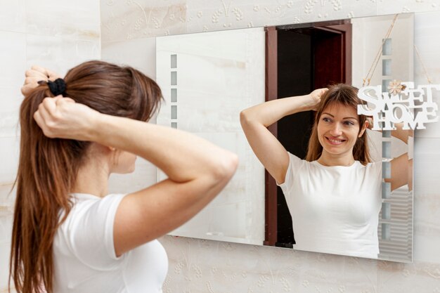 Bella donna che organizza i suoi capelli in specchio