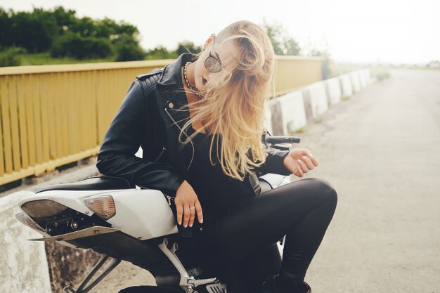 Bella donna che posa con gli occhiali da sole su una motocicletta