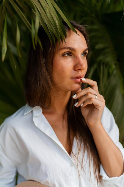 Bella donna che si gode le vacanze tropicali in Thailandia, indossa una camicetta bianca e posa sopra le palme.