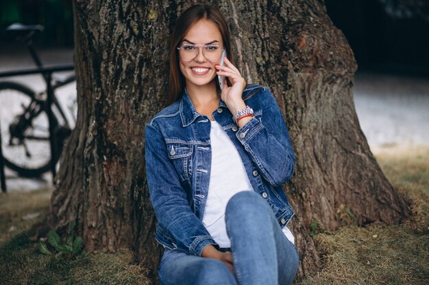 Bella donna che si siede sotto un albero e parlando al telefono