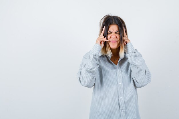 Bella donna che soffre di forte mal di testa in camicia e sembra angosciata, vista frontale.