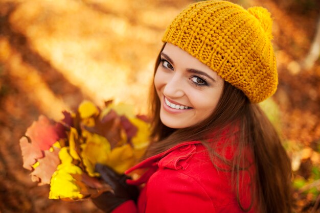 Bella donna che tiene le foglie nella soleggiata giornata autunnale