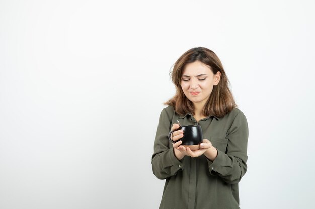 Bella donna che tiene tazza di caffè e in piedi sopra bianco. Foto di alta qualità