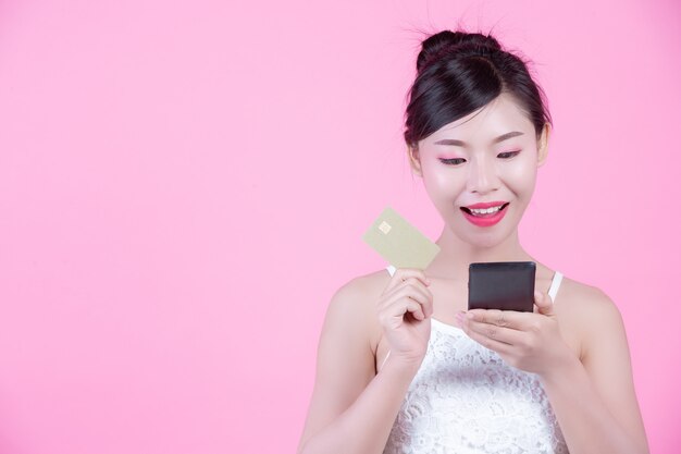 Bella donna che tiene uno smartphone e una carta su uno sfondo rosa