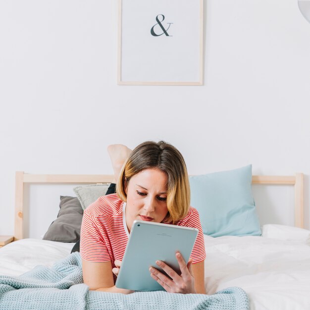 Bella donna che utilizza compressa sul letto