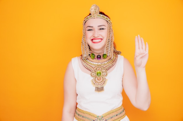 Bella donna come cleopatra in antico costume egiziano felice e allegro sorridente che mostra il numero quattro con le dita sull'arancia