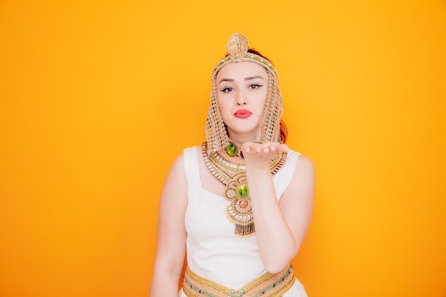 Bella donna come cleopatra in antico costume egiziano felice e positivo che invia un bacio d'aria sull'arancia