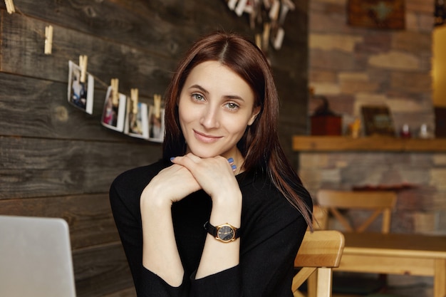 Bella donna con capelli castani e bel sorriso che guarda l'obbiettivo mentre ci si rilassa nell'accogliente caffetteria