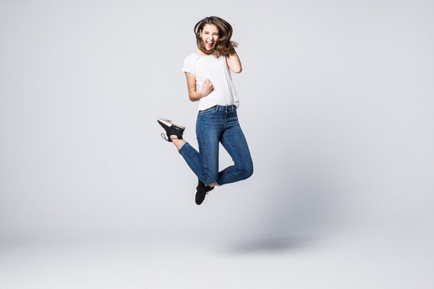 Bella donna con capelli lunghi castani e felice espressione facciale sorridente che salta in studio isolato su bianco