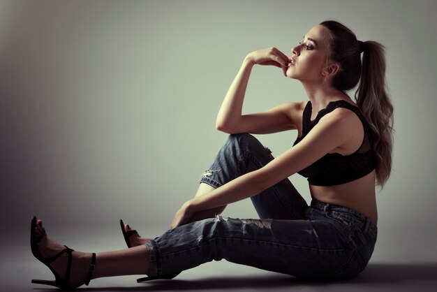 Bella donna con i capelli molto lunghi che indossa reggiseno nero e blue jeans seduti