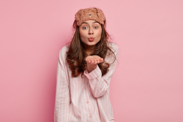 Bella donna con i capelli ricci, fa un bacio d'aria, indossa la maschera del sonno