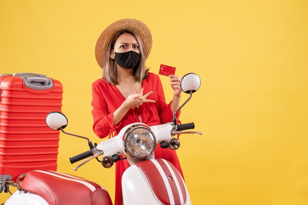 bella donna con maschera nera in possesso di carta di credito vicino al motorino